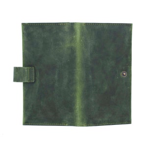 May include: Open, green leather journal with a button closure and a tab closure. The journal is made of a distressed leather material. The stitching is visible along the edges of the journal. The journal is open and ready to be used.