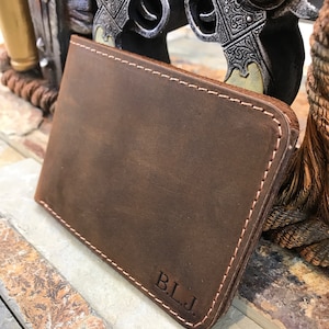 May include: A brown leather wallet with a stitched edge and the initials "B.L.J." embossed on the front.
