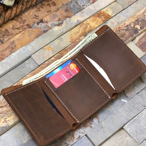 May include: A brown leather wallet with three card slots and a cash pocket. The wallet is open and has a credit card and cash inside.