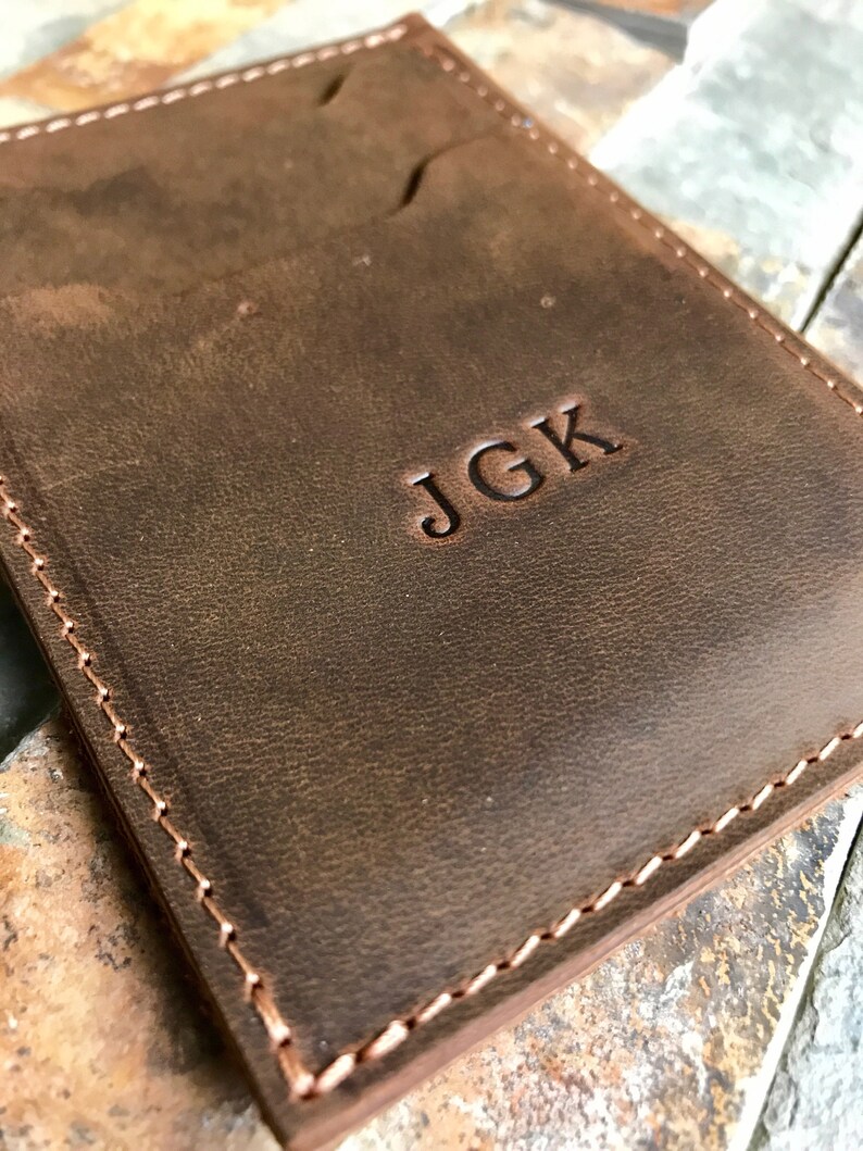 May include: A brown leather wallet with a stitched edge and the initials "JGK" embossed on the front.