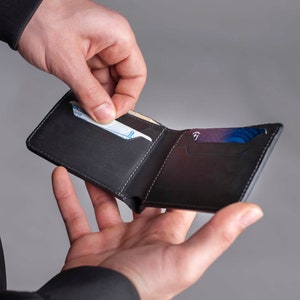 May include: A black leather wallet with a card slot and a billfold. The wallet is open and a credit card is being pulled out.