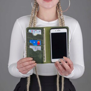 Puede incluir: Una funda de tel&eacute;fono de cuero verde con m&uacute;ltiples ranuras para tarjetas y un tel&eacute;fono en su interior. La funda est&aacute; abierta y el tel&eacute;fono es visible.