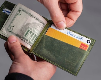 May include: A green leather wallet with a money clip, holding a five dollar bill and a credit card. The credit card has the text "Wisconsin" and "Wells Fargo" on it.