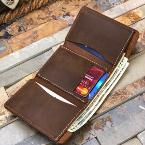May include: A brown leather wallet with multiple card slots and a billfold. The wallet is open and contains several credit cards and cash.