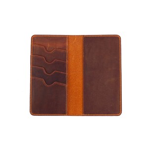 Puede incluir: Una cartera de cuero marr&oacute;n con m&uacute;ltiples ranuras para tarjetas y un portafolios. La cartera est&aacute; abierta para mostrar el interior.