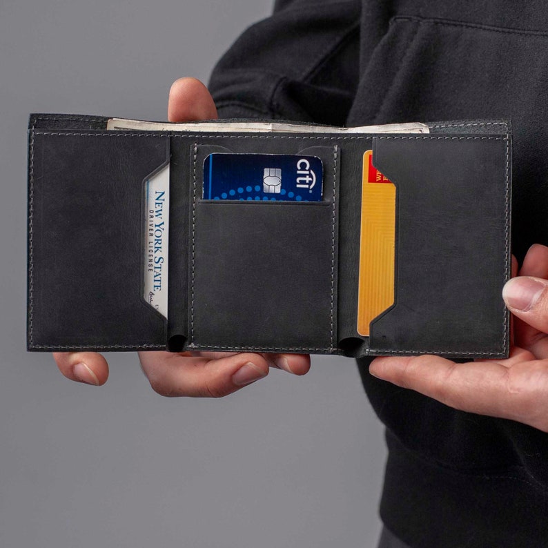 May include: A black leather wallet with multiple card slots, open to reveal a credit card, a driver's license, and a yellow card. The wallet has stitching around the edges.