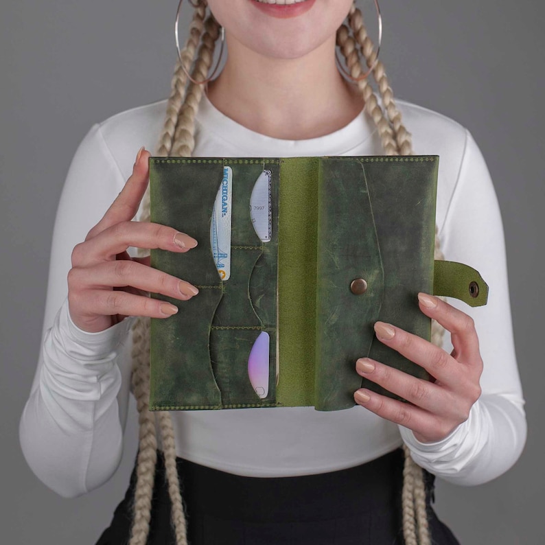 May include: Open, green leather wallet with multiple card slots and a snap closure. The wallet is held open, revealing the interior and the cards inside. The leather has a distressed finish, giving it a vintage look.