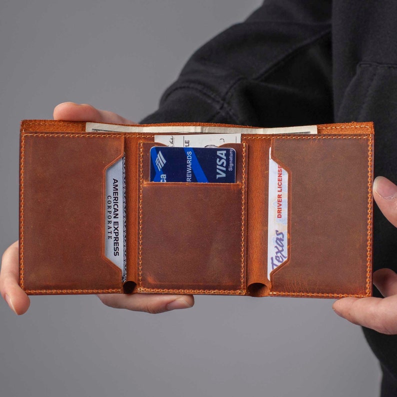 May include: A brown leather wallet with three card slots and a cash pocket. The wallet is open and shows a credit card, a driver's license, and cash.