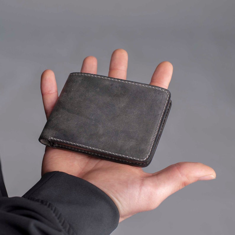 May include: A dark grey leather wallet with a stitched edge.