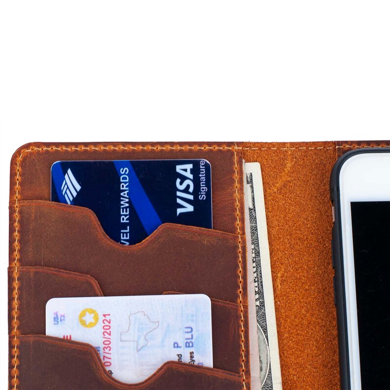 Puede incluir: Una cartera de cuero marr&oacute;n con m&uacute;ltiples ranuras para tarjetas y un soporte para tel&eacute;fono. La cartera tiene una tarjeta de cr&eacute;dito con el texto "Travel Rewards Visa Signature" insertada en una de las ranuras. Un billete es visible en la ranura para efectivo.