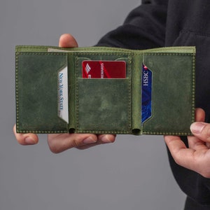 May include: A green leather wallet with two card slots and a billfold. The wallet is open and shows a red credit card with the text "REWARDS" and a blue credit card with the text "HSBC".
