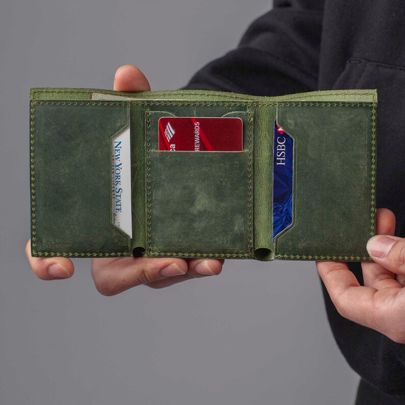 May include: A green leather wallet with two card slots and a billfold. The wallet is open and shows a red credit card with the text "REWARDS" and a blue credit card with the text "HSBC".