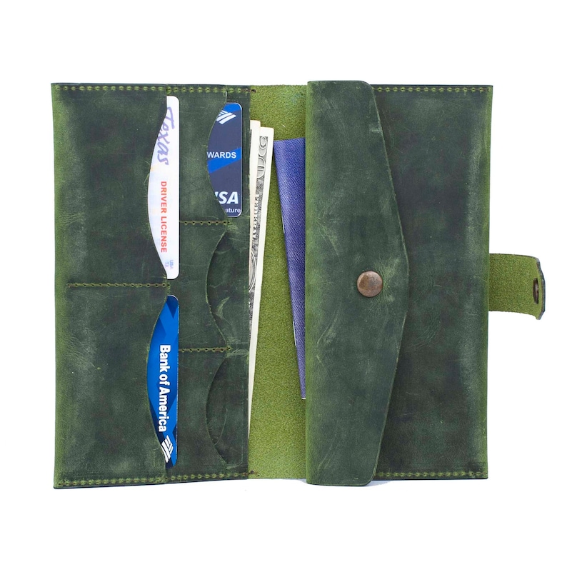 May include: Open green leather wallet with multiple card slots, holding a driver's license, credit cards, and cash. The wallet is open, revealing a passport and more storage. A snap closure secures the wallet.