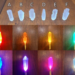 May include: Six clear crystal shapes with different angles and facets, illuminated with different coloured lights. The colours are red, orange, yellow, green, blue, and purple.