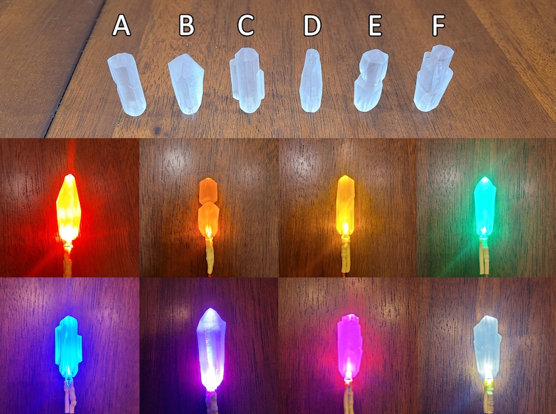 May include: Six clear crystal shapes with different angles and facets, illuminated with different coloured lights. The colours are red, orange, yellow, green, blue, and purple.