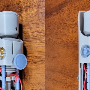 May include: A disassembled lightsaber with a grey plastic body, red and blue wires, and gold-coloured connectors. The lightsaber has a blue knob on the side and a grey plastic cap on the top.