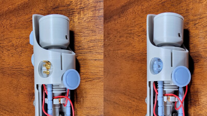 May include: A disassembled lightsaber with a grey plastic body, red and blue wires, and gold-coloured connectors. The lightsaber has a blue knob on the side and a grey plastic cap on the top.