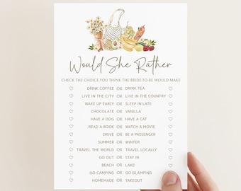May include: A printable bridal shower game card with the text "Would She Rather" and a list of questions for guests to guess the bride's preferences. The card features a watercolor illustration of a picnic basket with fruit and vegetables.