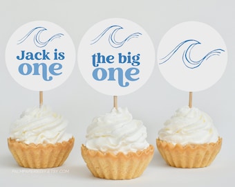 May include: Three cupcakes with blue and white wave themed toppers. The toppers say "Jack is one", "the big one", and a single wave.
