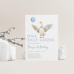 Op de afbeelding: Een blauwe en witte verjaardagsuitnodiging met een aquarel-illustratie van een gans die een blauwe strik draagt en een blauwe ballon vasthoudt. De tekst luidt "One Silly Goose" en "Bunny's 1st Birthday".
