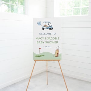 May include: Welcome to Macy & Jacob's Baby Shower sign with a blue golf cart, green golf course, and golf clubs. The date is 8.10.2022.