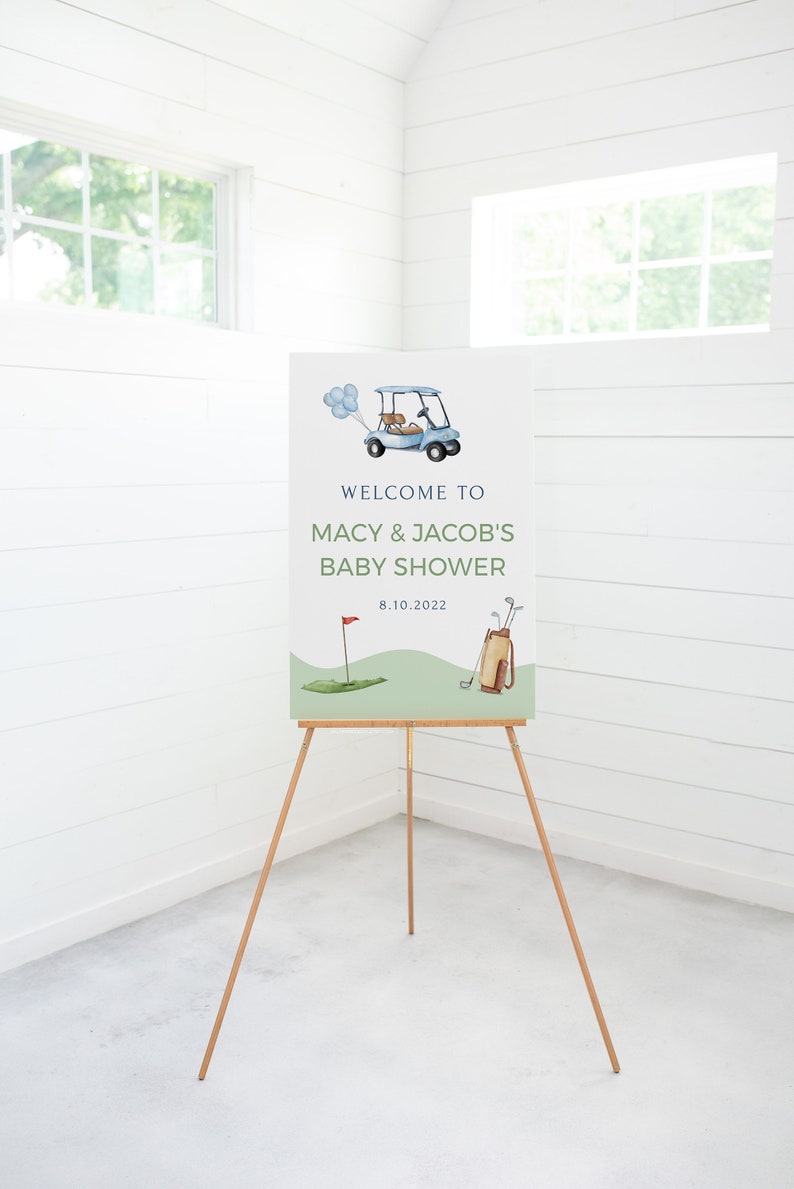 May include: Welcome to Macy & Jacob's Baby Shower sign with a blue golf cart, green golf course, and golf clubs. The date is 8.10.2022.