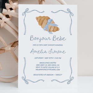 May include: A blue and white baby shower invitation with a croissant illustration and the text "Bonjour Bebe", "Join us for a baby shower honoring Amelia Simone", "Saturday May 10th 12:00 PM", "Madeleines Bistro", "5555 Baby Ln, San Diego, CA", "RSVP to Katie Collins by 5.1", "Palmpaperiediy@gmail.com", and "Registered at Amazon + Target".