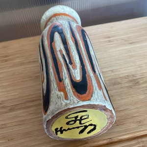 May include: A white ceramic vase with black and orange abstract designs. The vase has a yellow sticker on the bottom with black writing that says "GE HH 7".