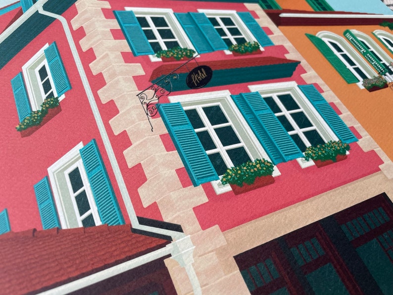 Detail view of an art print depicting the colourful buildings of Alsace, France, adorned with flowers on a cobble stone street.