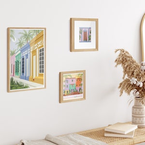 A collection of Venezuelan art prints in the form of a gallery wall featuring a beach, a colonial style window and houses in Maracaibo.