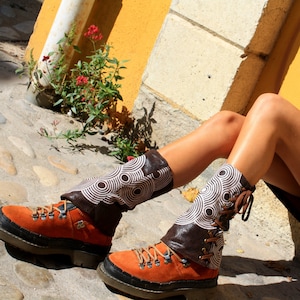 May include: A pair of brown leather boots with white and black patterned fabric gaiters. The boots have laces and are worn by a person sitting on a wall.