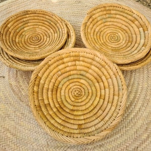 May include: Set of four woven straw plates with a circular design. The plates are made of natural materials and have a light brown color.