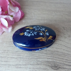 Può includere: Una scatola portaoggetti in porcellana blu e bianca con un motivo floreale. La scatola è di forma ovale e ha un bordo dorato.