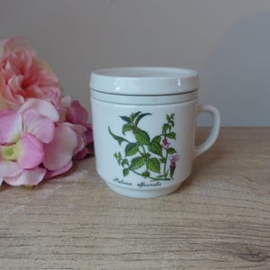 Puede incluir: Taza de té de cerámica blanca con tapa, con una ilustración botánica verde y rosa de Melissa officinalis, un tipo de menta.
