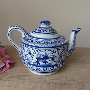 Könnte beinhalten: Eine weiße Keramik-Teekanne mit aufwendigen, handgemalten blauen Mustern, darunter florale Motive und eine kleine Hirschfigur. Die Teekanne hat einen passenden Deckel mit Knauf, einen geschwungenen Griff und einen Ausguss mit blauen Linien.