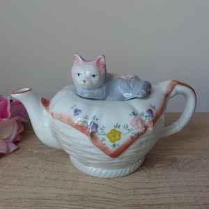 Mały porcelanowy czajnik w kształcie kota leżący na kocu w koszyku, czajnik w kształcie kota, kolekcja Vintage