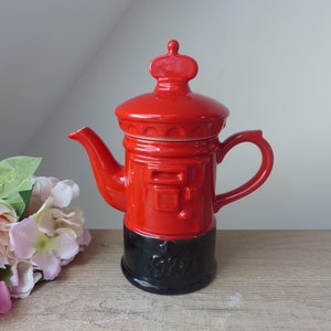 Peut inclure: Théière en céramique rouge en forme de boîte aux lettres britannique avec une base noire. La théière a une couronne sur le couvercle.