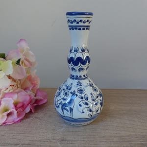 May include: A white ceramic vase with a blue and white floral design. The vase has a bulbous body and a narrow neck.