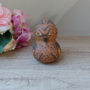 Peut inclure: Une figurine de hibou en céramique peinte à la main avec des motifs marrons et noirs. Le hibou a de grands yeux ronds et un petit bec. La figurine est posée sur une surface en bois clair.