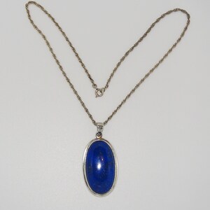 Op de afbeelding: Een zilveren ketting met een hanger met een grote ovale lapis lazuli-steen.