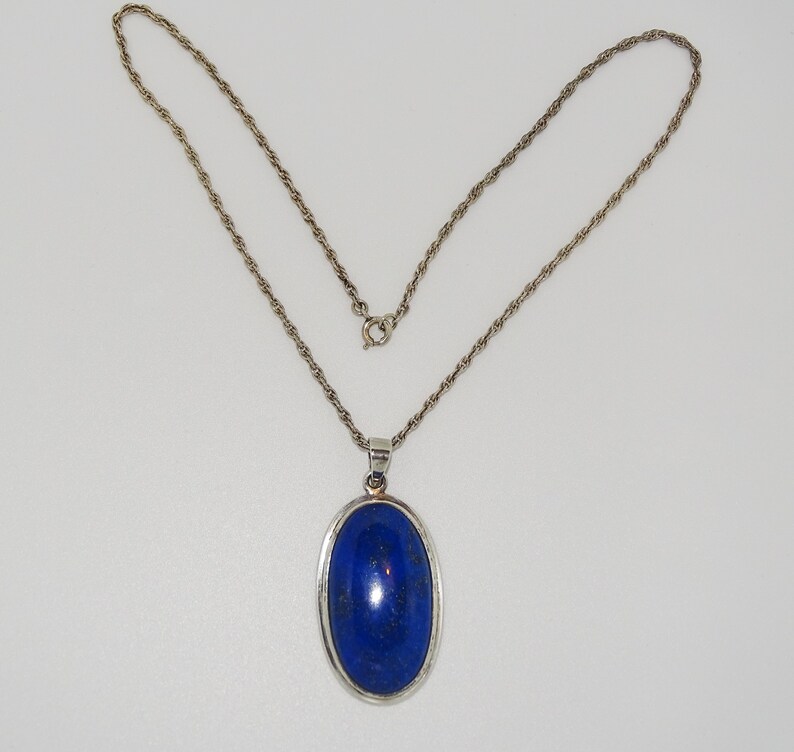 Op de afbeelding: Een zilveren ketting met een hanger met een grote ovale lapis lazuli-steen.