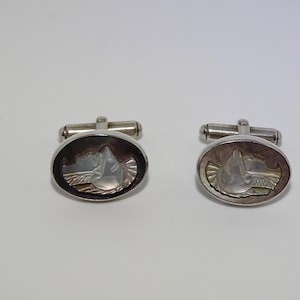 May include: A pair of silver cufflinks with oval-shaped mother-of-pearl inlays. The inlays feature a carved design of a stylized animal head.