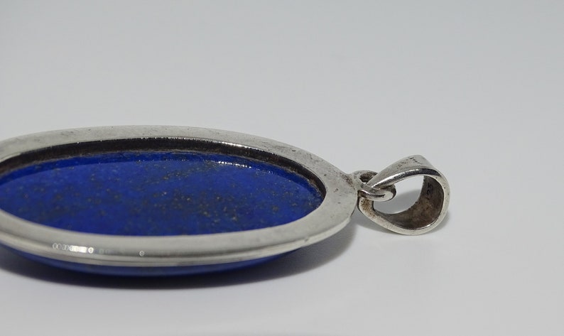 Op de afbeelding: Een zilveren hanger met een blauwe ovale lapis lazuli-steen.