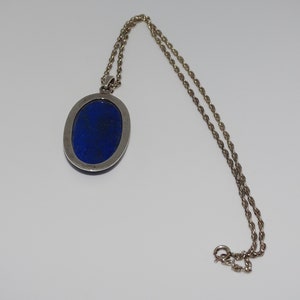 Op de afbeelding: Een zilveren ketting met een hanger met een grote ovale lapis lazuli-steen.