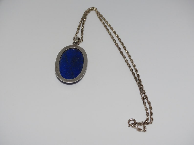 Op de afbeelding: Een zilveren ketting met een hanger met een grote ovale lapis lazuli-steen.