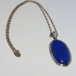 Op de afbeelding: Een zilveren ketting met een grote ovale hanger met een donkerblauwe lapis lazuli-steen.