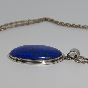 Op de afbeelding: Een zilveren ketting met een grote ovale hanger met een blauwe lapis lazuli-steen.