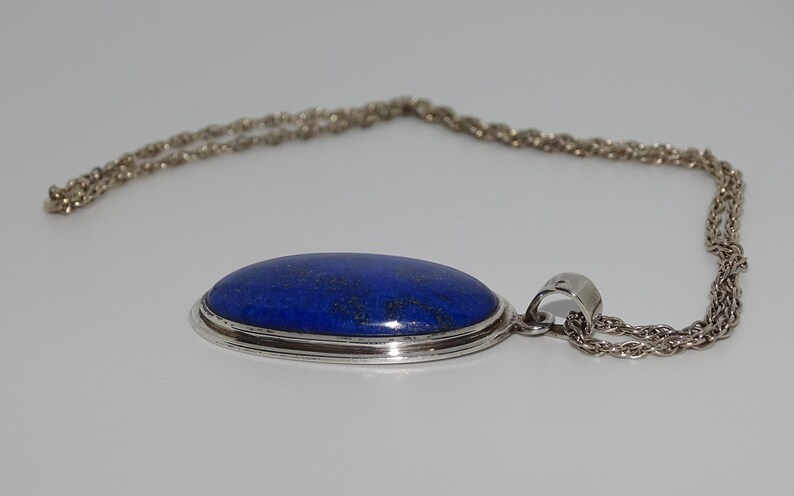 Op de afbeelding: Een zilveren ketting met een grote ovale hanger met een blauwe lapis lazuli-steen.