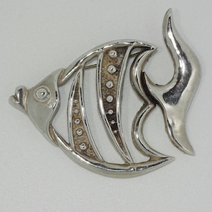 Op de afbeelding: Een zilverkleurige vis broche met een gedetailleerd ontwerp. De vis heeft een getextureerd lichaam en een gladde, gebogen staartvin.
