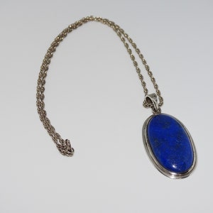 Op de afbeelding: Een zilveren ketting met een grote ovale hanger met een diepblauwe lapis lazuli-steen.